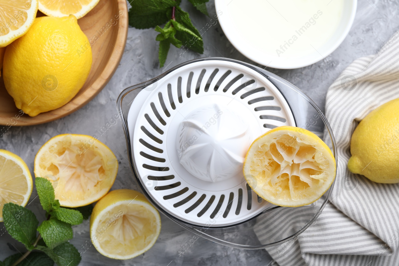 Photo of Juicer, fresh juice, lemons and mint on grey table, top view