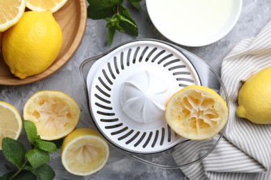 Juicer, fresh juice, lemons and mint on grey table, top view