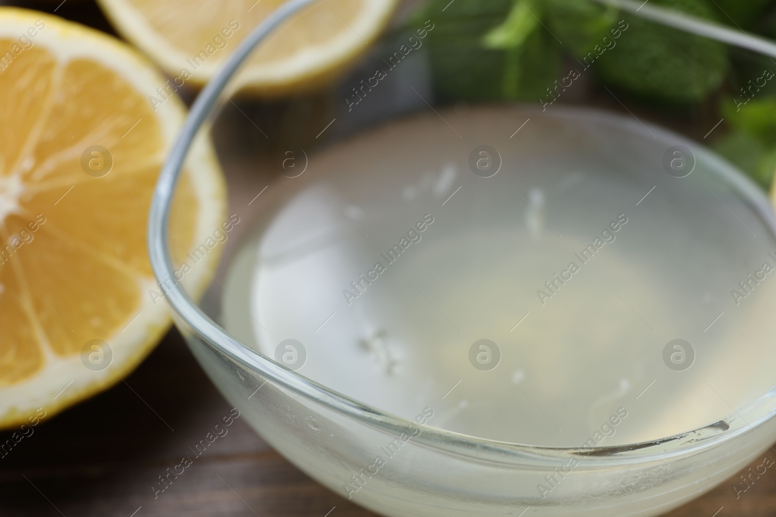 Photo of Fresh lemon juice in bowl and fruit on table, closeup