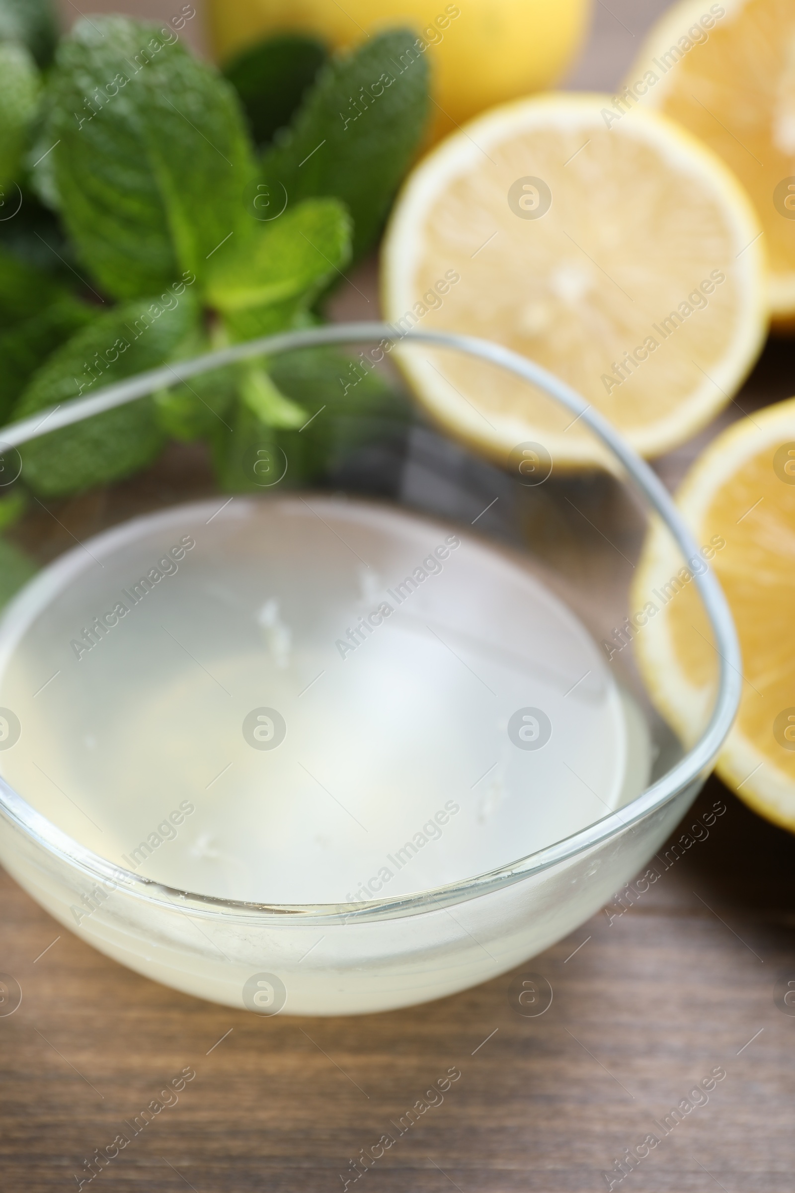 Photo of Fresh lemon juice in bowl, fruits and mint on wooden table, closeup