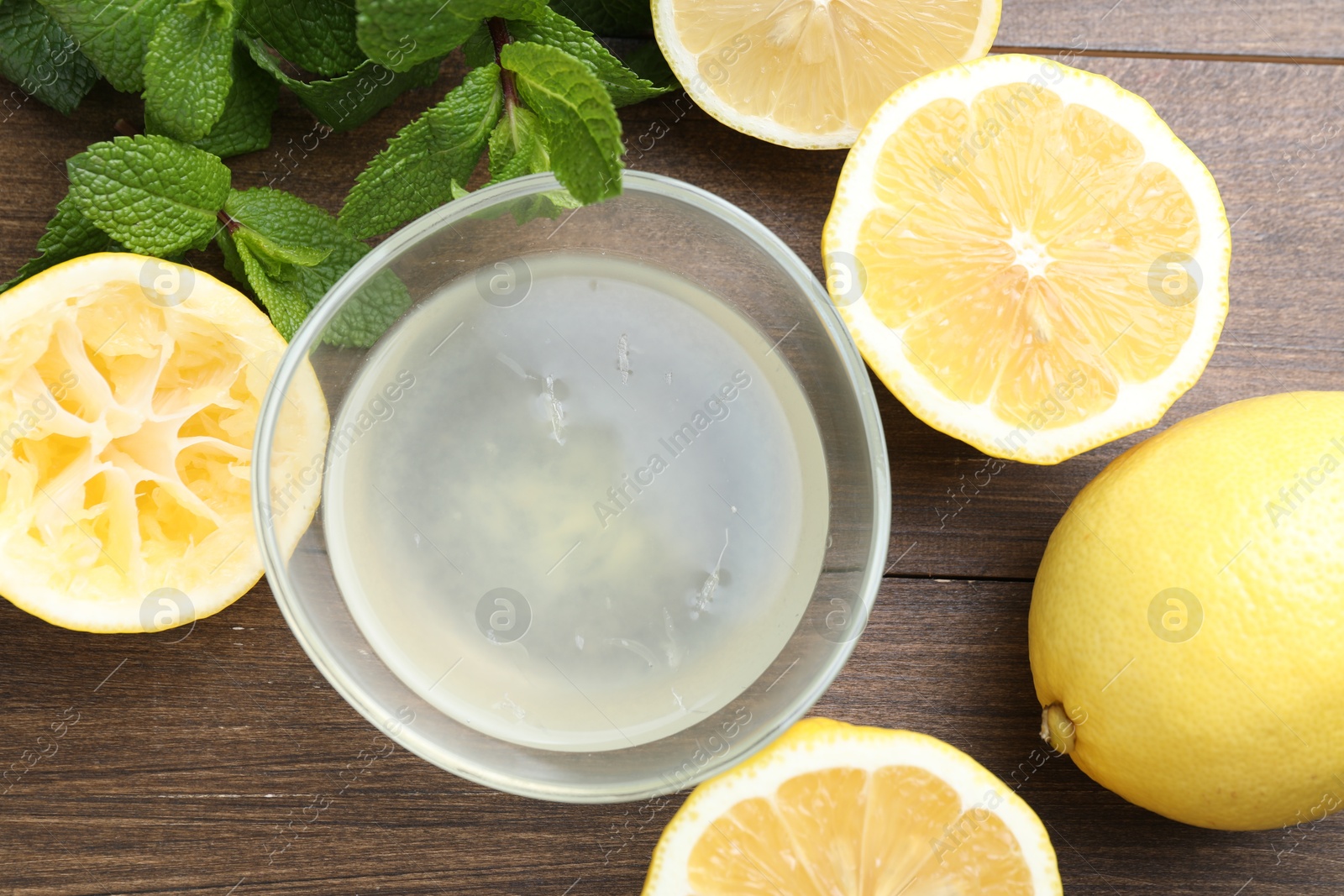 Photo of Fresh lemon juice in bowl, fruits and mint on wooden table, top view