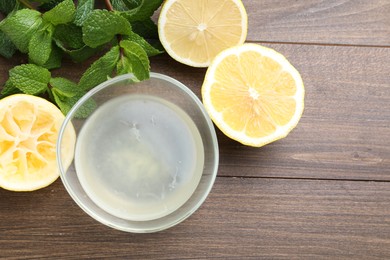 Photo of Fresh lemon juice in bowl, fruits and mint on wooden table, top view