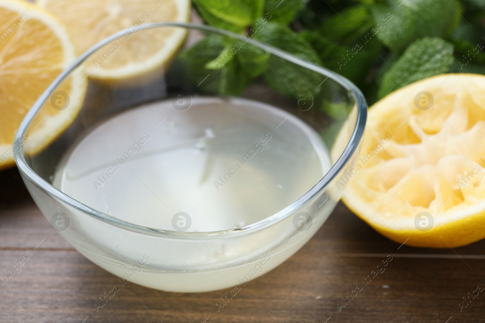 Photo of Fresh lemon juice in bowl, fruits and mint on wooden table, closeup