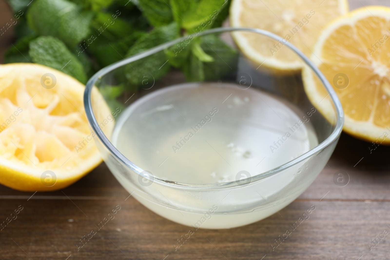 Photo of Fresh lemon juice in bowl, fruits and mint on wooden table, closeup