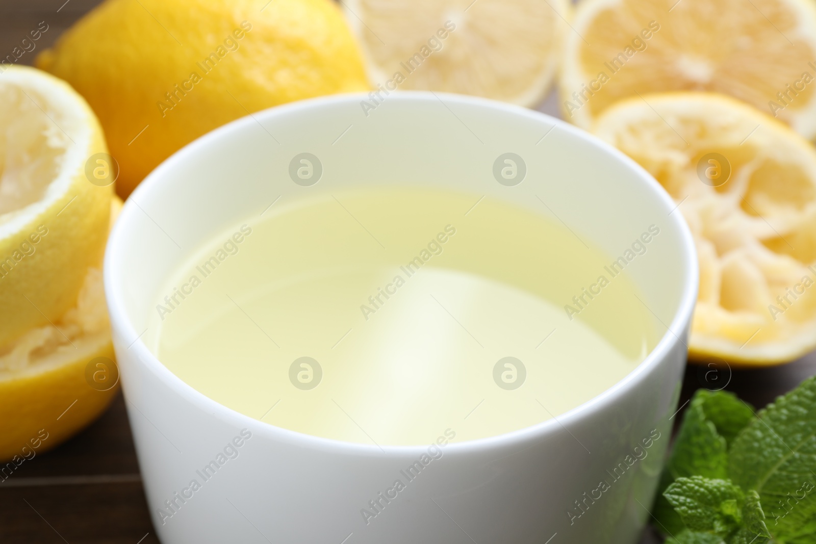 Photo of Fresh lemon juice in bowl, fruits and mint on table, closeup