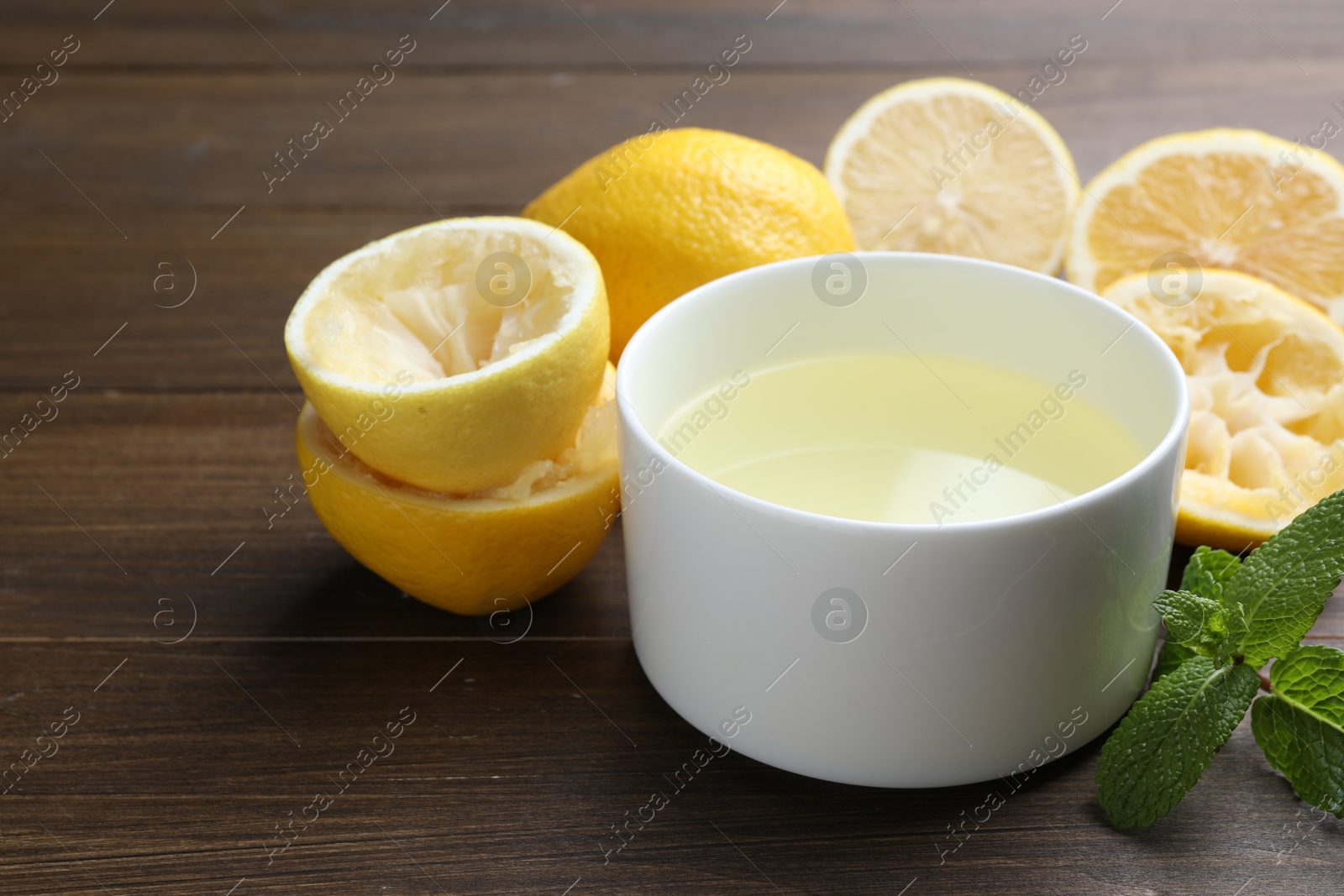 Photo of Fresh lemon juice in bowl, fruits and mint on wooden table, closeup