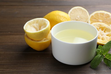 Photo of Fresh lemon juice in bowl, fruits and mint on wooden table, closeup