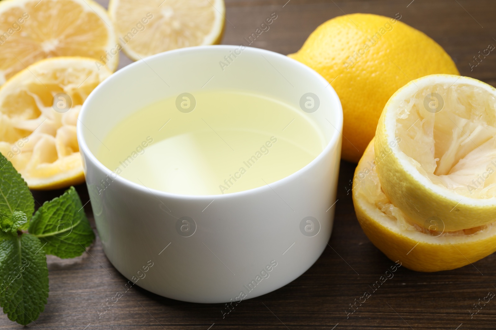 Photo of Fresh lemon juice in bowl, fruits and mint on wooden table, closeup