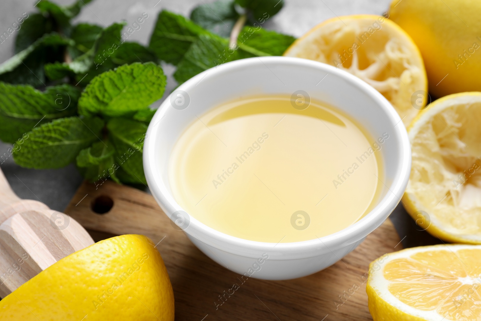 Photo of Fresh lemon juice in bowl, lemons and mint on table, closeup