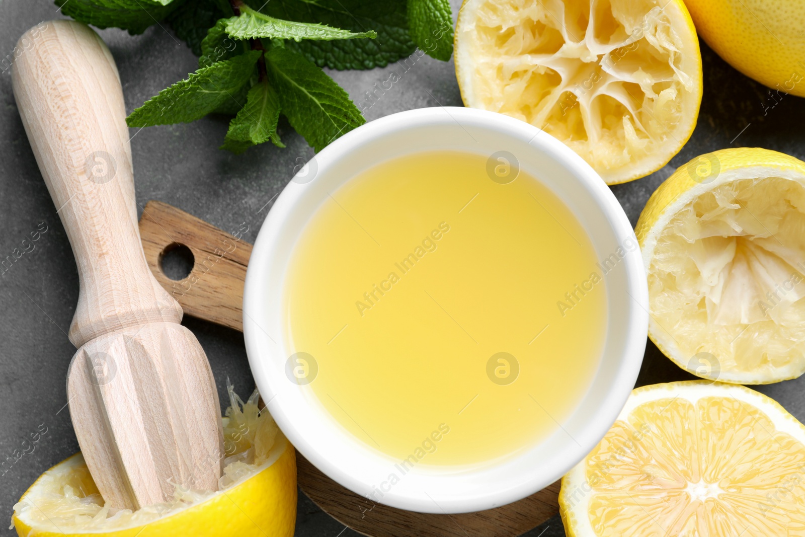 Photo of Fresh lemon juice in bowl, lemons, squeezer and mint on grey table, top view