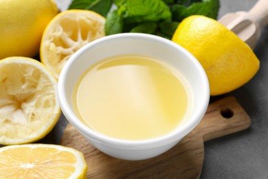 Photo of Fresh lemon juice in bowl, fruits and mint on grey table, closeup