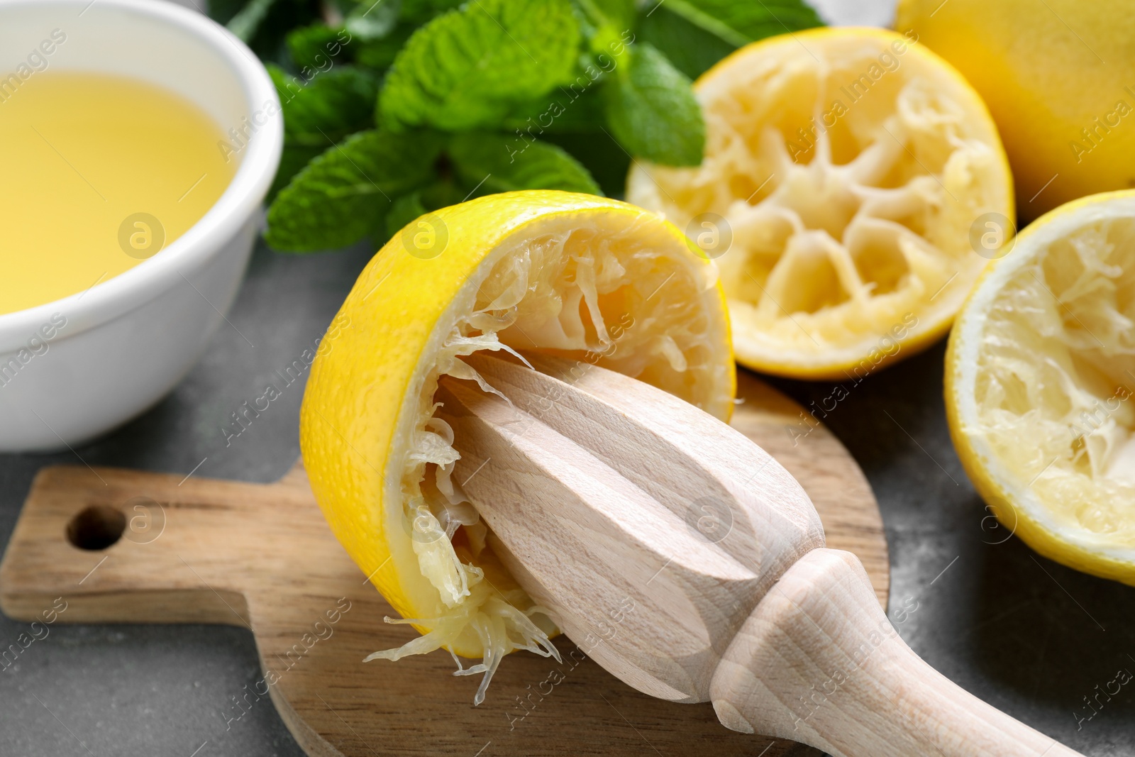 Photo of Wooden squeezer, lemons, juice and mint on grey table, closeup