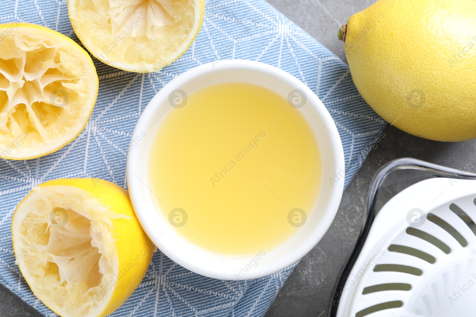 Photo of Fresh lemon juice in bowl and fruits on grey table, top view