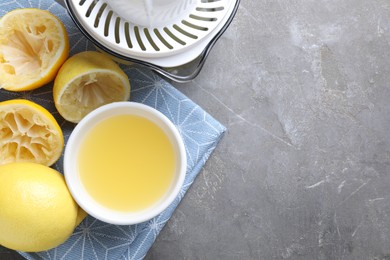 Photo of Fresh lemon juice in bowl, fruits and juicer on grey table, top view. Space for text