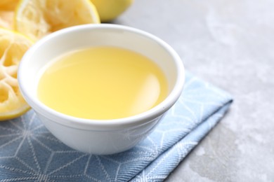 Photo of Fresh lemon juice in bowl and fruit on grey table, closeup