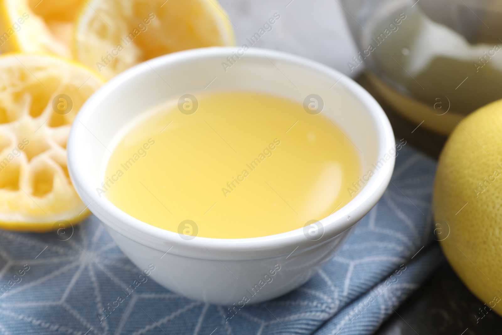 Photo of Fresh lemon juice in bowl and fruits on table, closeup