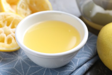 Fresh lemon juice in bowl and fruits on table, closeup