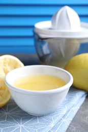 Photo of Fresh lemon juice in bowl, fruits and juicer on table, closeup