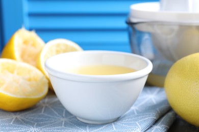 Fresh lemon juice in bowl and fruits on table, closeup