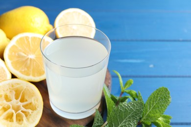 Photo of Fresh juice in glass, lemons and mint on blue wooden table, closeup. Space for text