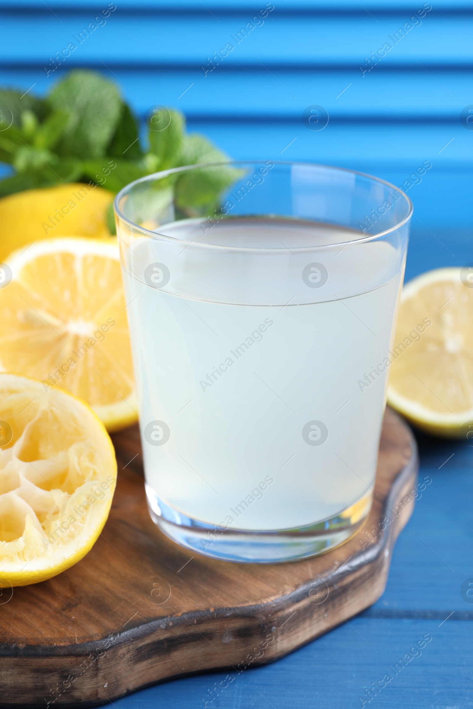 Photo of Fresh juice in glass and lemons on blue wooden table, closeup