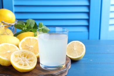 Photo of Fresh juice in glass, lemons and mint on blue wooden table. Space for text