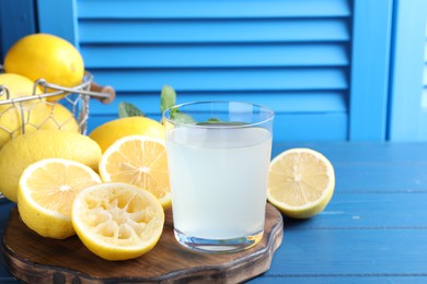 Photo of Fresh juice in glass and lemons on blue wooden table. Space for text