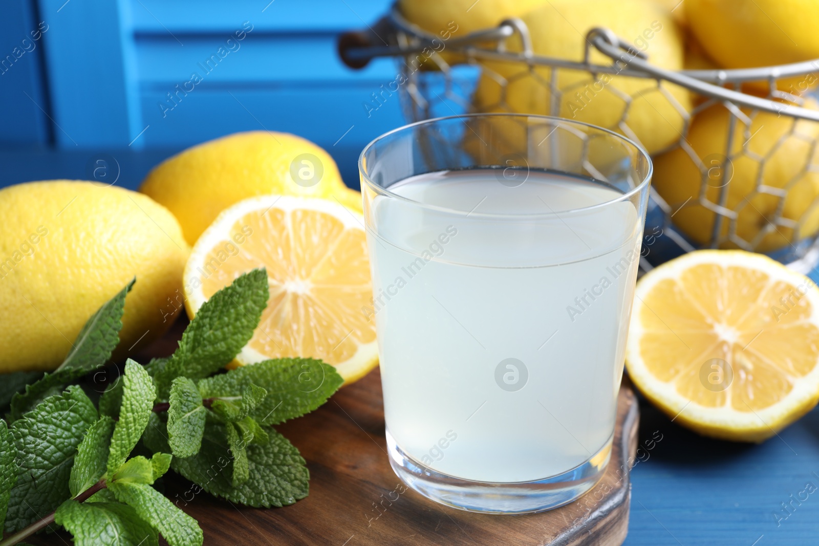 Photo of Fresh juice in glass, lemons and mint on blue table, closeup