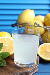 Photo of Fresh juice in glass, lemons and mint on blue wooden table, closeup