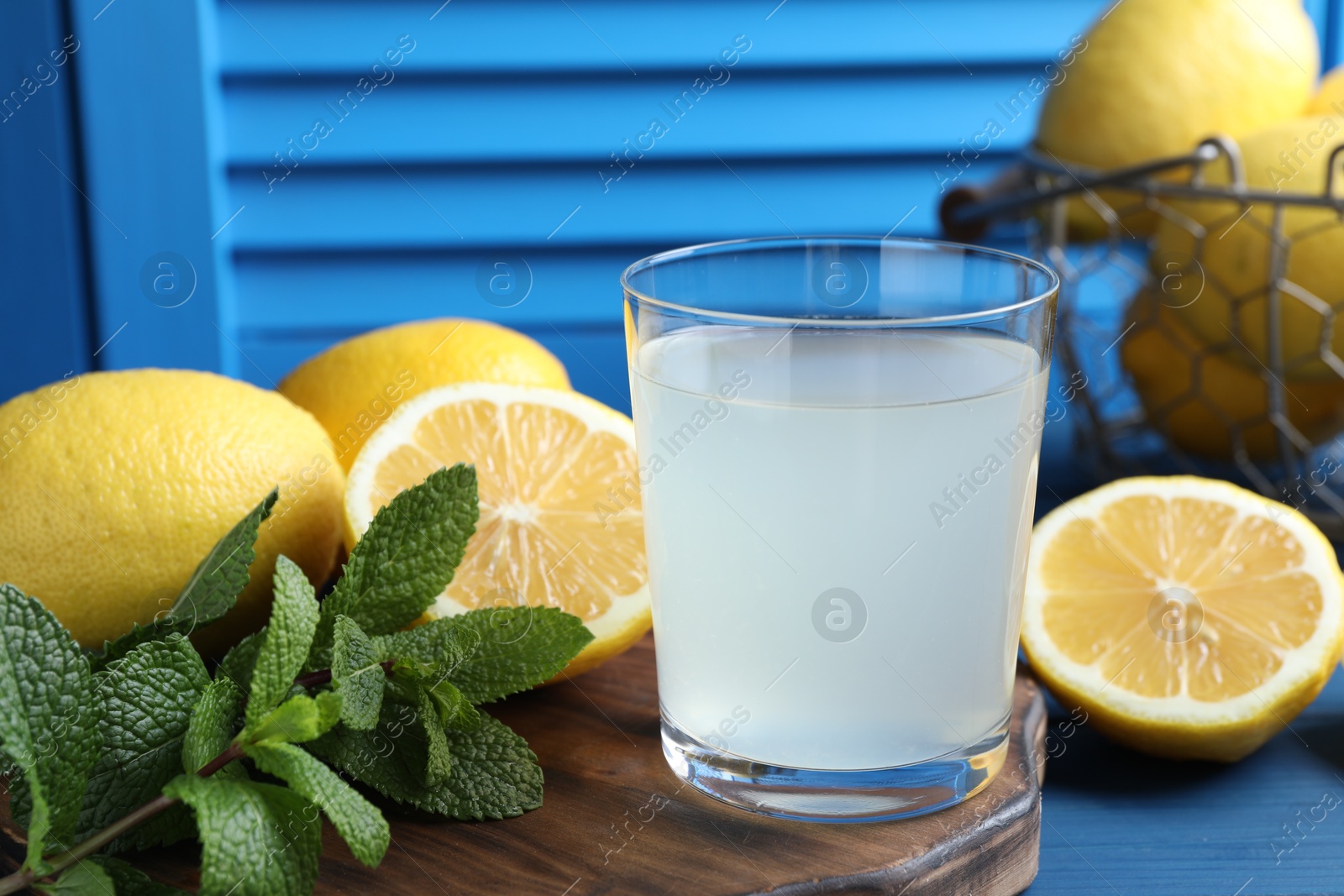 Photo of Fresh juice in glass, lemons and mint on blue wooden table, closeup