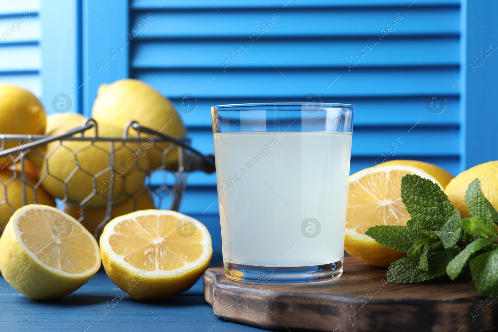 Photo of Fresh juice in glass, lemons and mint on blue wooden table