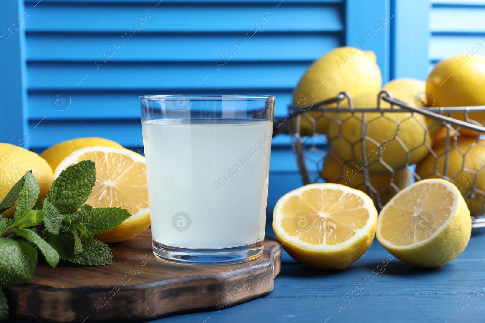 Photo of Fresh juice in glass, lemons and mint on blue wooden table