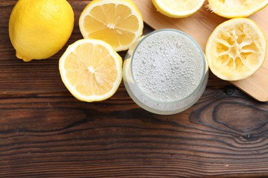 Photo of Fresh juice in glass and lemons on wooden table, top view