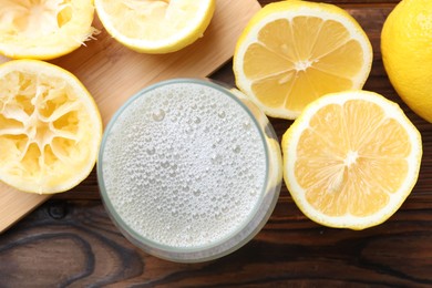 Photo of Fresh juice in glass and lemons on wooden table, top view