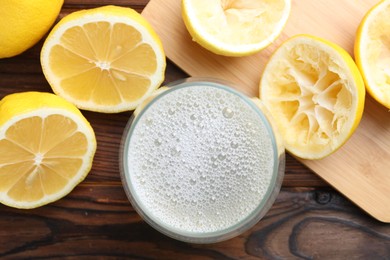 Photo of Fresh juice in glass and lemons on wooden table, top view