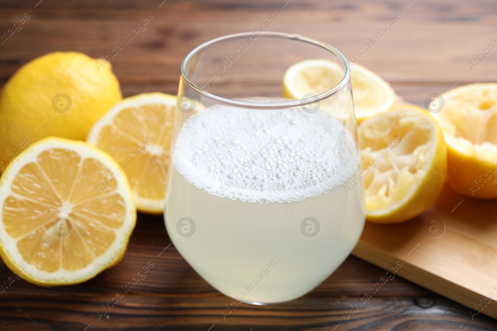 Photo of Fresh juice in glass and lemons on wooden table, closeup