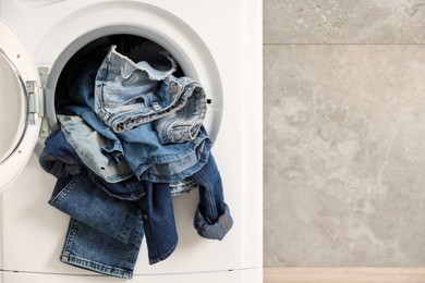 Photo of Washing machine with dirty jeans and other denim clothes indoors, space for text