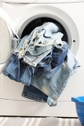 Photo of Washing machine with dirty jeans and other denim clothes indoors