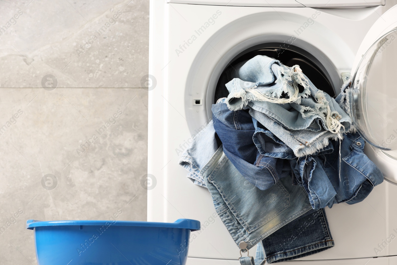 Photo of Washing machine with dirty jeans and other denim clothes indoors, space for text