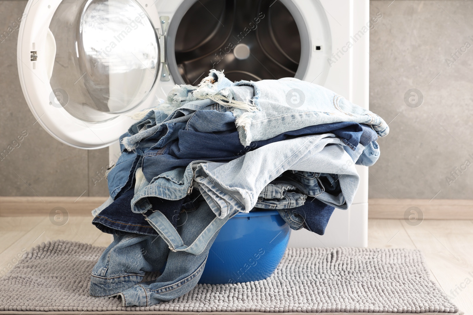 Photo of Washing machine and laundry basket with dirty denim clothes indoors