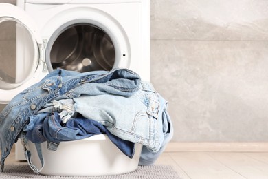 Photo of Washing machine and laundry basket with dirty denim clothes indoors, space for text