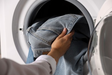 Photo of Woman putting dirty jeans and other denim clothes into washing machine, closeup