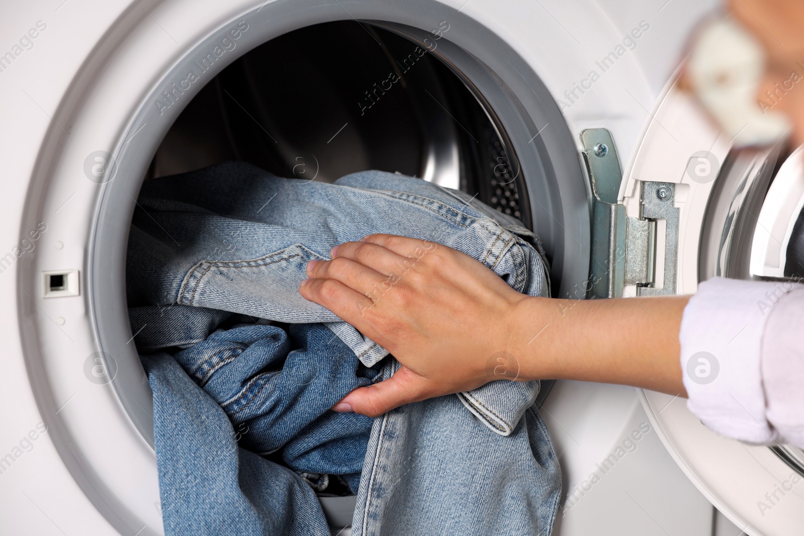 Photo of Woman putting dirty jeans and other denim clothes into washing machine, closeup