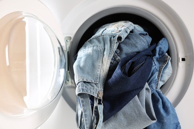 Washing machine with dirty jeans and other denim clothes indoors, closeup