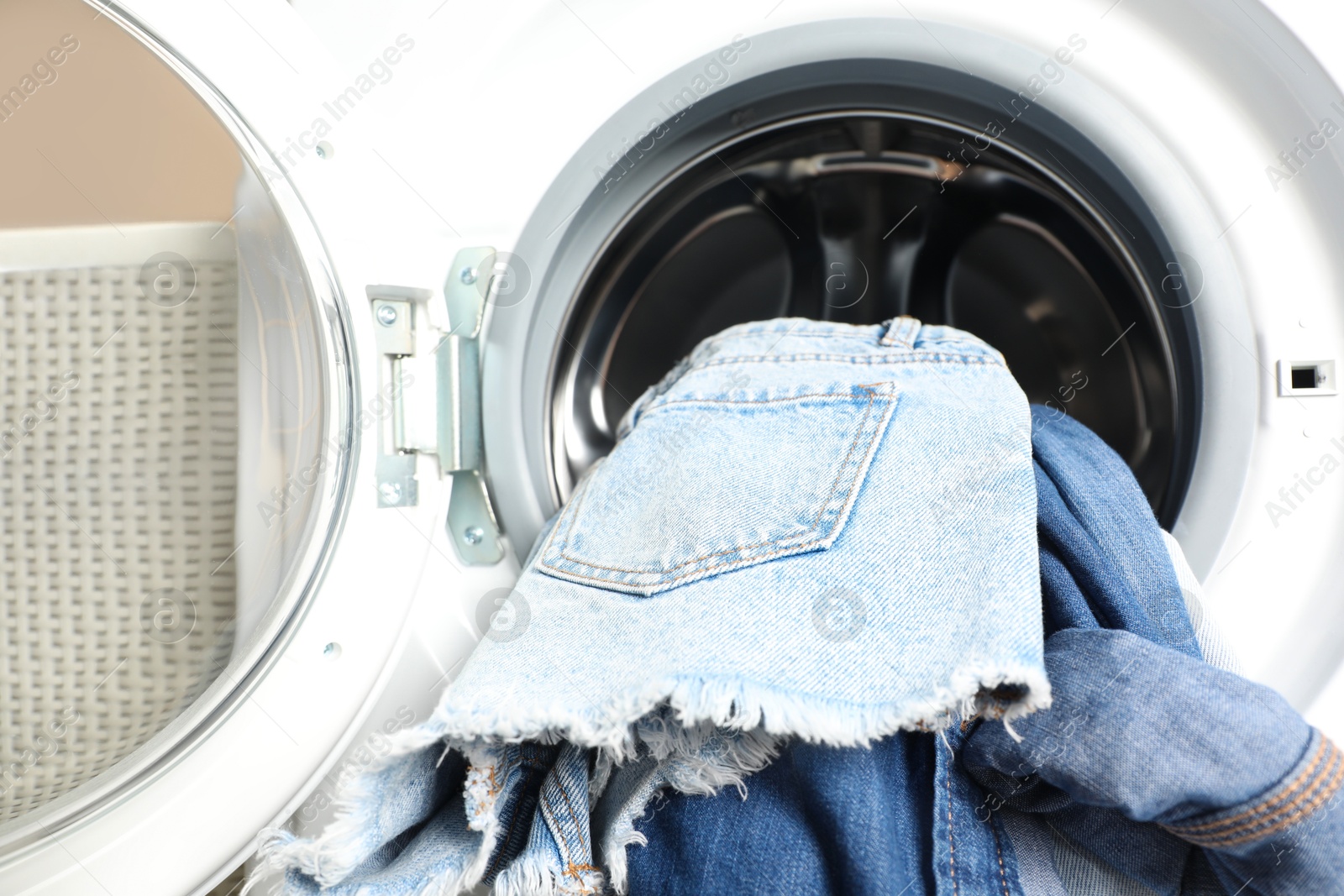 Photo of Washing machine with dirty jeans and other denim clothes indoors, closeup