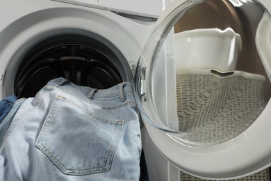 Photo of Washing machine with dirty jeans and other denim clothes indoors, closeup