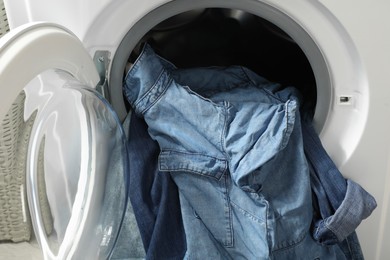 Photo of Washing machine with dirty jeans and other denim clothes indoors