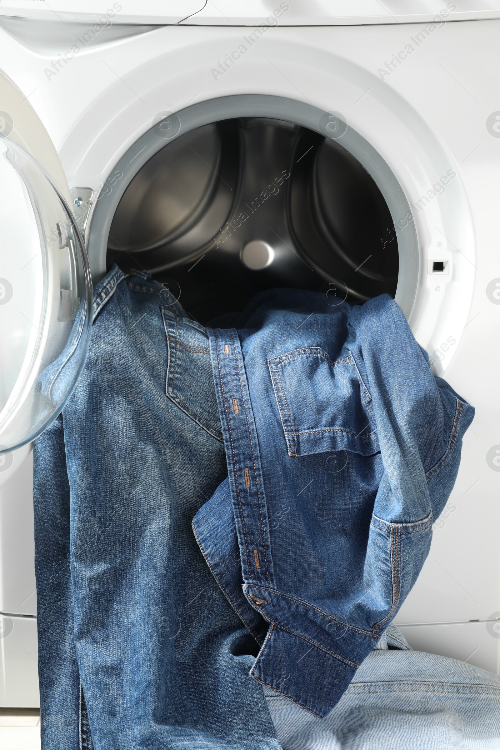 Photo of Washing machine with dirty jeans and other denim clothes indoors