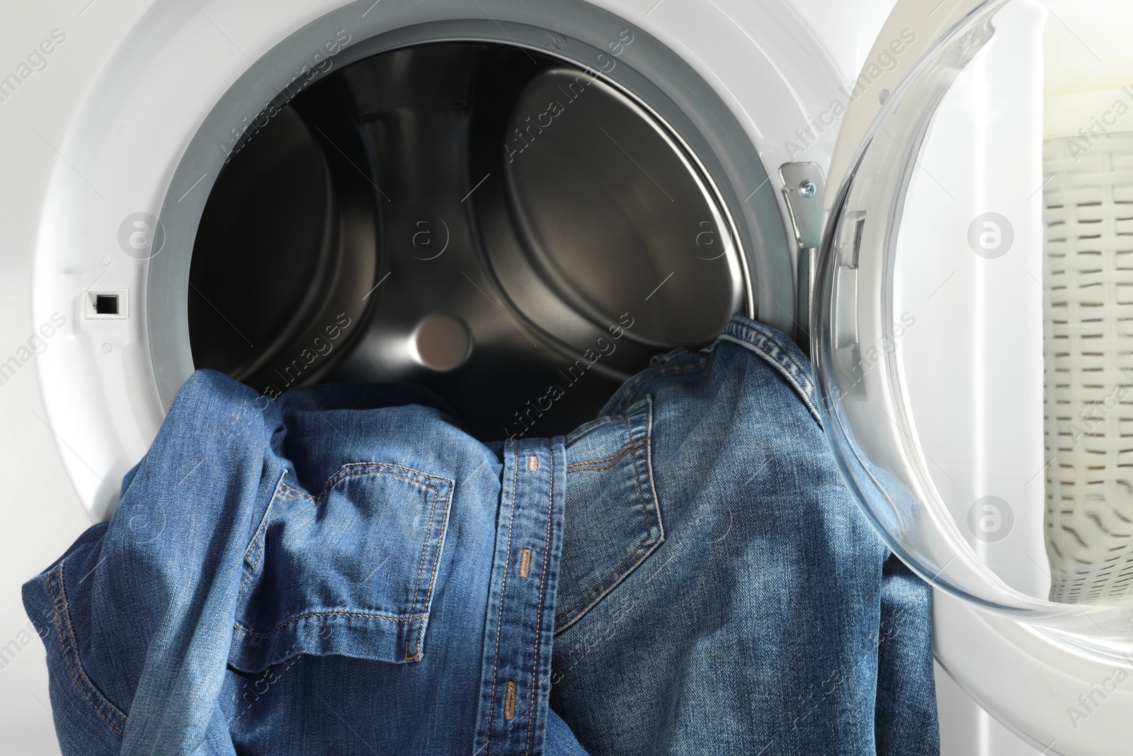 Photo of Washing machine with dirty jeans and other denim clothes indoors, closeup