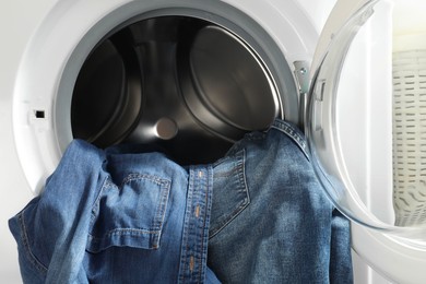 Washing machine with dirty jeans and other denim clothes indoors, closeup